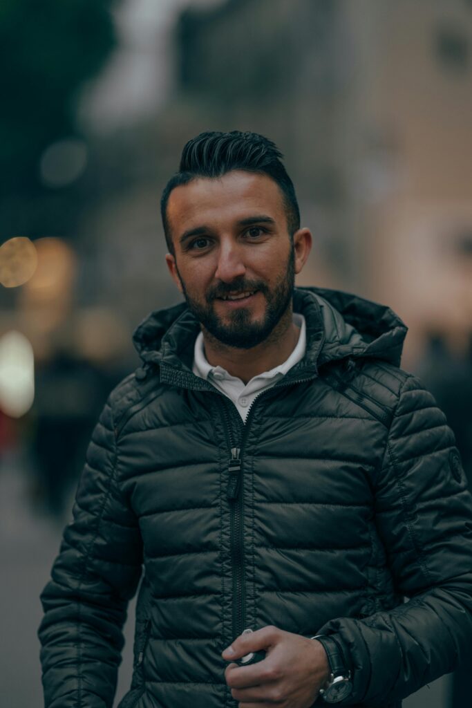Cheerful bearded male in autumn jacket standing in city street and looking at camera